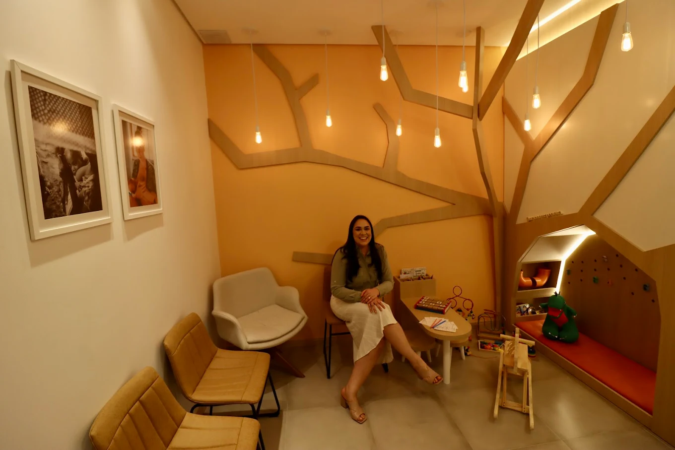 Sala de espera com poltronas, quadros e árvore cenográfica iluminada