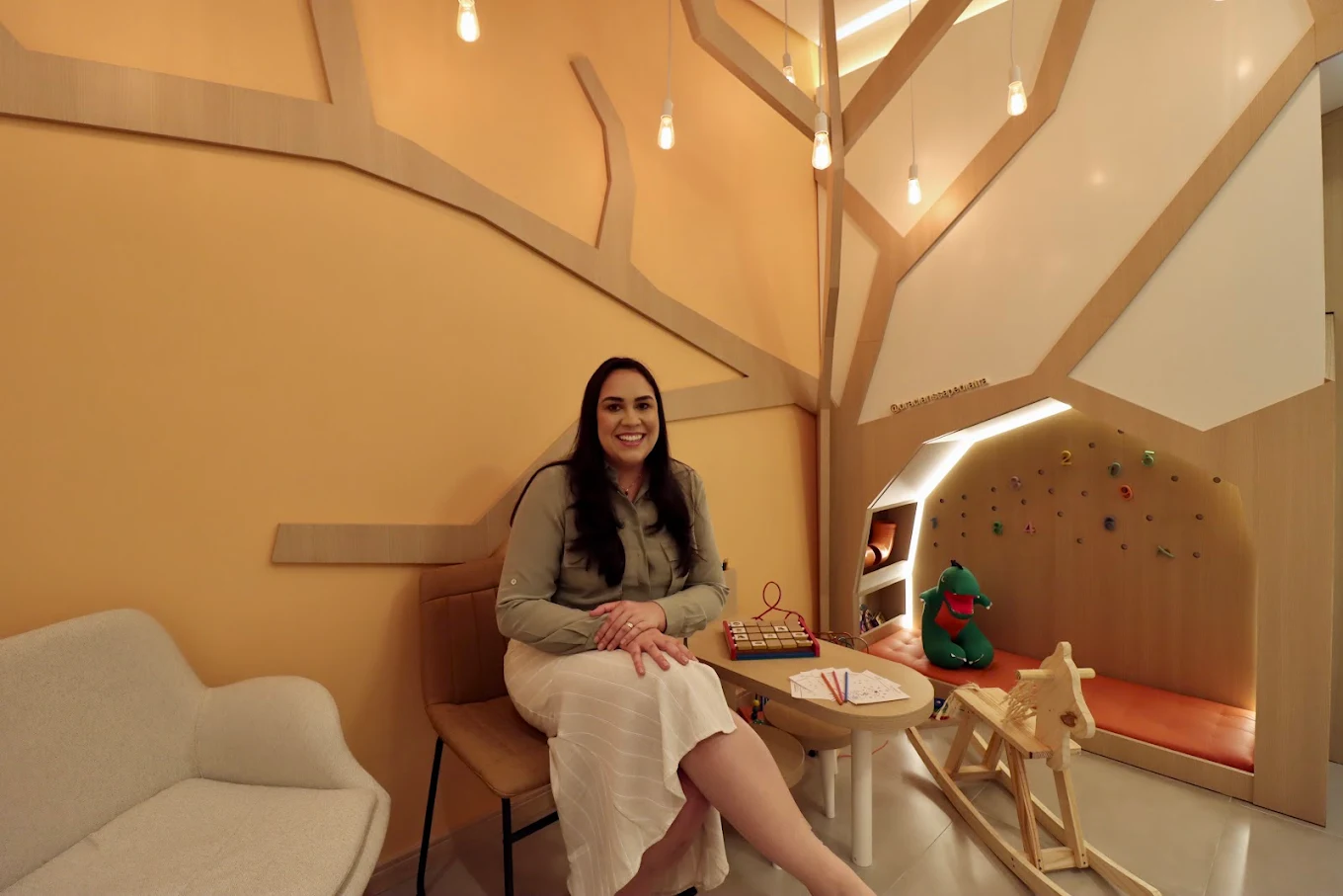 Dra. Clarissa no espaço lúdico com mesa infantil e parede sensorial