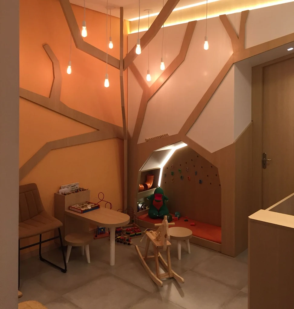 Espaço lúdico com árvore cenográfica e luminárias suspensas